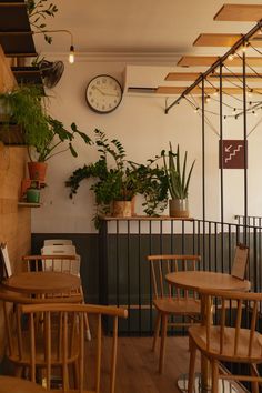 there are many wooden chairs and tables in this restaurant with plants on the wall behind them