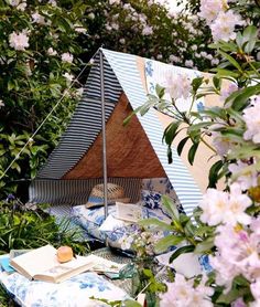 a tent in the middle of some trees with flowers around it and books on top