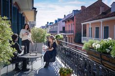 two women sitting at a table on a balcony with potted plants in front of them