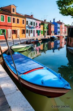 a row of boats sitting next to each other on a river in front of colorful buildings