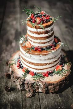 a three tiered cake with berries and greenery sits on top of a tree stump