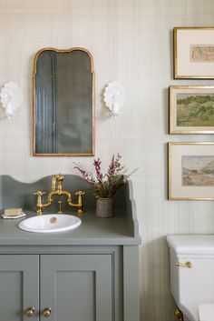 a bathroom with a sink, toilet and pictures on the wall above it's mirror