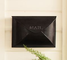 a black mailbox mounted to the side of a white wall next to a plant