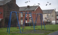 an empty playground with swings and birds flying over it in front of some brick buildings