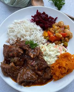 a white plate topped with meat, rice and veggies on top of a table