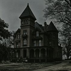 an old house with a clock tower in the front yard and dark skies above it