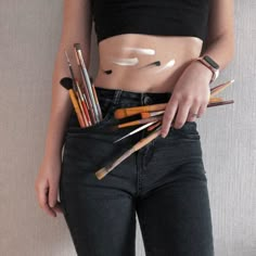 a woman is showing off her stomach with pencils in her pocket and makeup brushes in her pockets