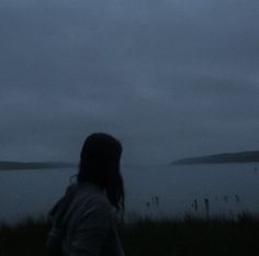 a woman standing in front of a body of water under a cloudy sky with an airplane flying overhead