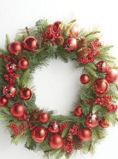 a christmas wreath hanging on the wall with ornaments and pine cones around it's edges