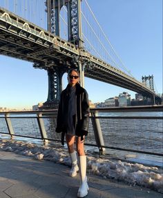 a woman standing in front of the manhattan bridge wearing white socks and knee high boots