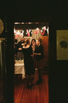 two women standing in front of a table with food on it and people looking at them through an open door