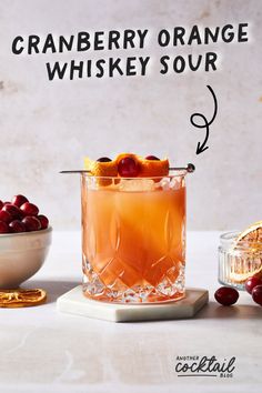 a cranberry orange whiskey sour cocktail in a glass with cherries around it