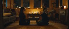 two people sitting on the floor in front of a coffee table with lit candles behind them