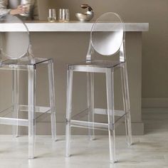 two clear bar stools sitting in front of a white counter with silverware on it