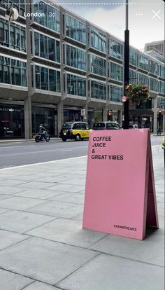 a pink sign sitting on the side of a road next to a street light and tall buildings