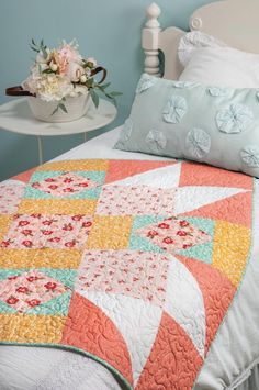 a bed with a quilt on top of it next to a night stand and flowers