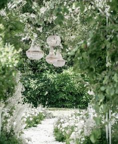 two wicker lamps hanging from the ceiling in a garden with white flowers and greenery