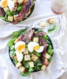 a salad with bacon, eggs and spinach leaves on a plate next to a cup of coffee