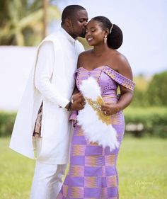 a man and woman standing next to each other in front of a lush green field