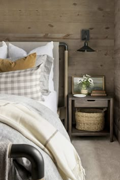 a bed in a bedroom with wooden walls and pillows on the headboard, next to a night stand