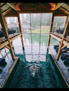 an indoor swimming pool surrounded by wooden beams and glass walls, with a person in the water