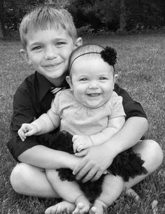 two children are sitting on the grass and smiling at the camera with their arms around each other