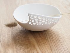 a white bowl sitting on top of a wooden table next to a yellow thread in it