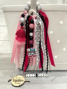 the pink and black bracelets are hanging from a white tote bag with tassels on it