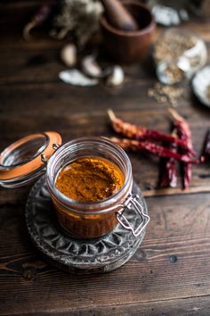 a glass jar filled with curry sitting on top of a wooden table next to other spices