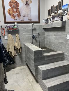 there is a dog sitting on the stairs in this bathroom with grey tile walls and flooring