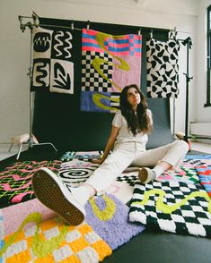 a woman is sitting on the floor in front of many quilts and rugs