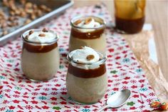 three jars filled with dessert sitting on top of a red and white table cloth next to spoons