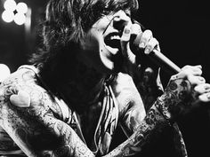 a man with tattoos on his arms holding a microphone in front of him and singing into the microphone