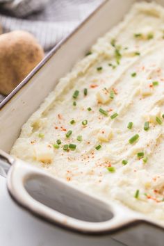 a casserole dish with mashed potatoes and scallions in the background