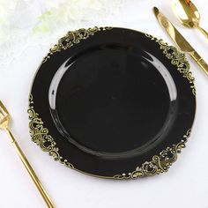 a black plate with gold trim sits on a white table cloth next to golden utensils