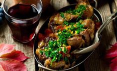 a bowl filled with meat and vegetables next to a glass of wine on top of a wooden table