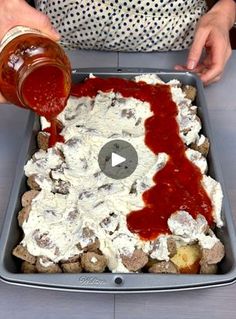 a person pouring ketchup on top of food in a baking pan with potatoes and meatballs