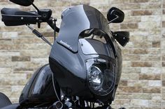 the front view of a black motorcycle parked in front of a brick wall with its lights on