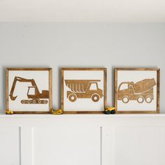 three framed pictures with construction vehicles are on a mantel in front of a white wall