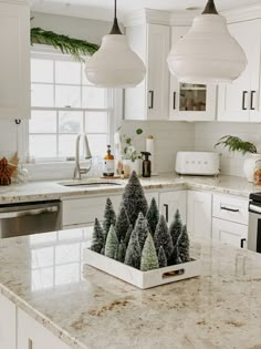 a kitchen with white cabinets and marble countertops has christmas trees in the centerpiece