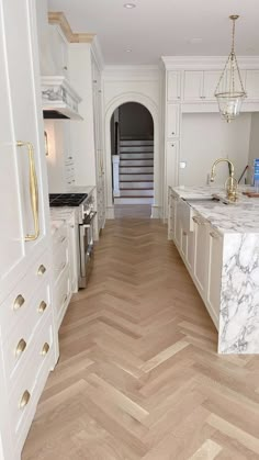 a large kitchen with white cabinets and marble counter tops, along with herringbone wood flooring