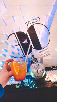 a person holding an orange drink in front of a sign with the word studio on it