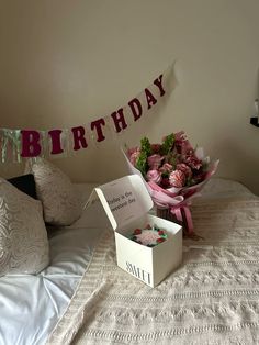 a birthday card in a box sitting on a bed with pink flowers and pillows next to it