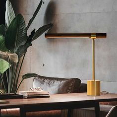 a table lamp sitting on top of a wooden table next to a chair and potted plant