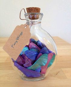 a glass bottle filled with purple and blue feathers on top of a wooden table next to a tag