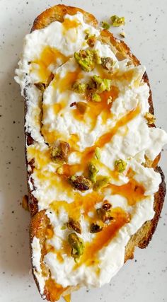 a piece of bread with whipped cream and pistachio toppings, on a white plate