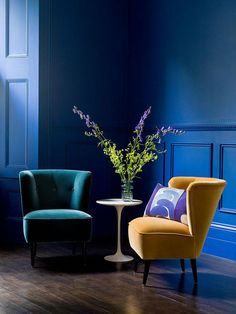 two chairs and a table in a room with blue walls, one has a flower vase on it