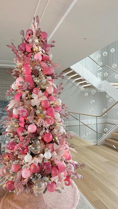 a pink christmas tree in the middle of a room with stairs and glass balconies