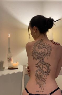 a woman with a dragon tattoo on her back is standing in front of a mirror