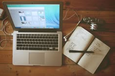 an open laptop computer sitting on top of a wooden desk next to a note book